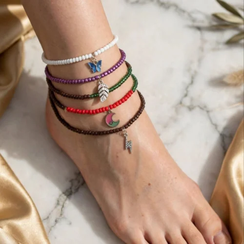 Five seed bead anklets in white, purple, green, red and brown with butterfly, leaf, moon and lightning charms on an ankle