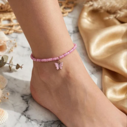 Pink pearlescent seed bead anklet with a pink butterfly charm worn on an ankle on white marble