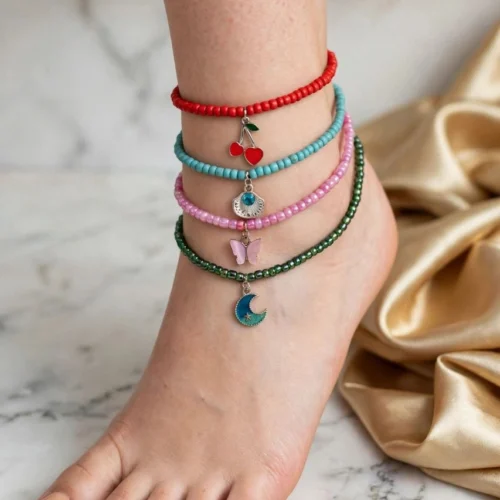 Four seed bead anklets in red, turquoise, pink and green with cherry, shell, butterfly and moon charms on an ankle