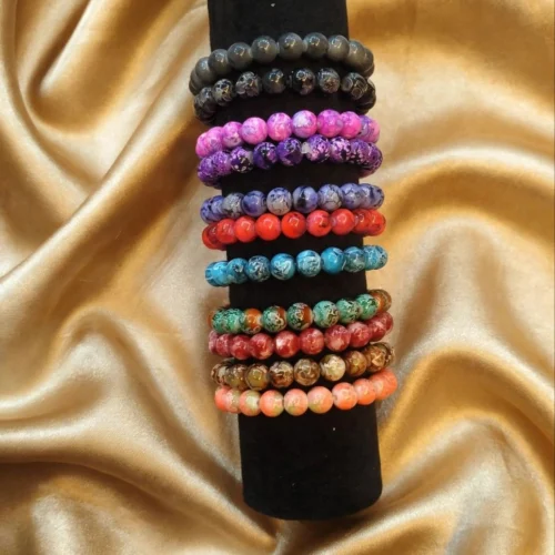 Stack of marbled round bead stretch bracelets in black, pink, purple, blue, red, turquoise, green, brown and coral on a black display