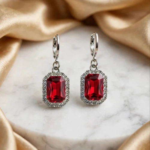 Red octagon crystal drop earrings with clear rhinestone halo on silver-tone huggie hoops on a marble plate