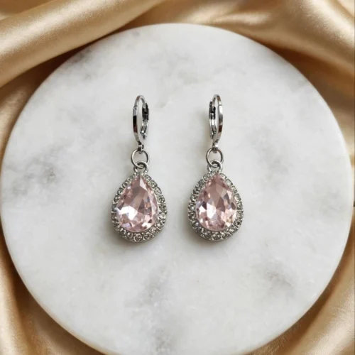 Blush pink teardrop crystal earrings framed with clear rhinestones on silver-tone huggie hoops on a round marble board