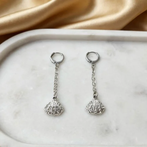 Silver-tone rhinestone scallop shell earrings on fine chain drops with huggie hoops on an oval marble tray