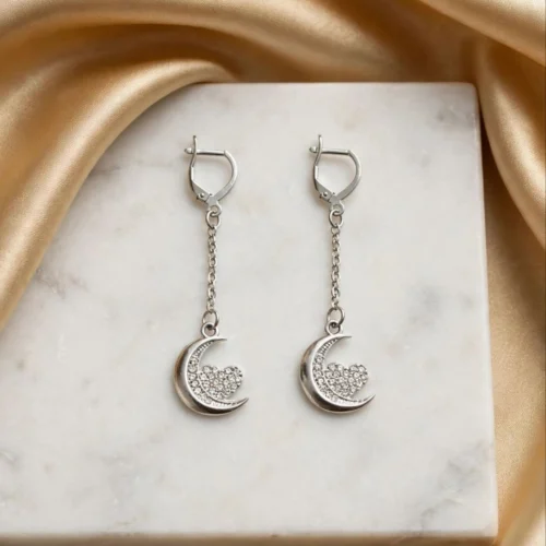 Long silver-tone crescent moon earrings with rhinestone heart on fine chains with leverback hooks on a marble board