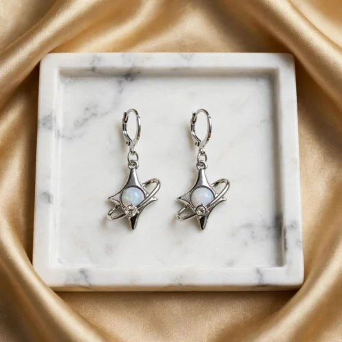 Silver-tone four-point star earrings with orbit ring, white opal-look stone and rhinestone on huggie hoops in a square marble tray
