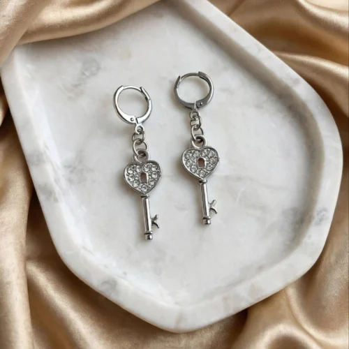 Silver-tone heart key earrings with clear rhinestones and keyhole on huggie hoops on a white marble tray