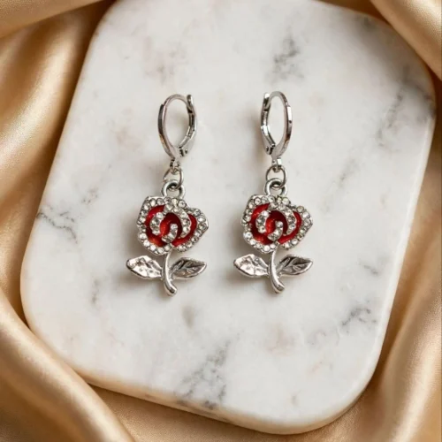 Silver-tone rose earrings with red enamel and rhinestone petals and leaves on huggie hoops on a marble board