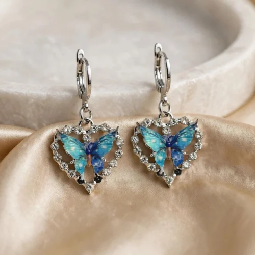 Silver-tone open heart earrings with clear rhinestones and blue turquoise enamel butterflies on huggie hoops on satin