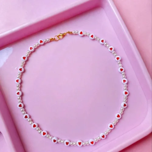 Choker necklace of white beads with red hearts and small faux pearls with gold-tone lobster clasp on a pink tray