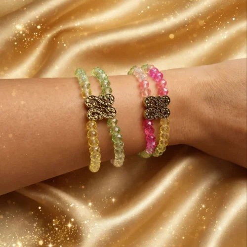 Two double-strand faceted crystal bead bracelets in green-yellow and pink-yellow with antique gold-tone filigree links on a wrist