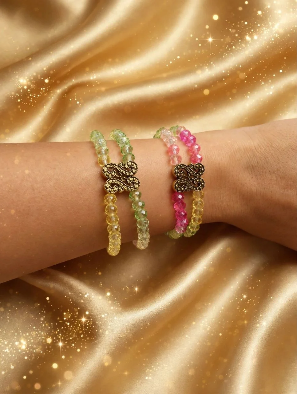 Two double-strand faceted crystal bead bracelets in green-yellow and pink-yellow with antique gold-tone filigree links on a wrist