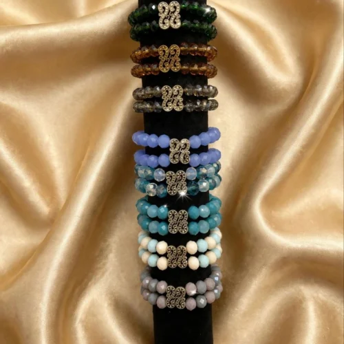 Double-strand faceted bead bracelets with filigree centre links in green, amber, grey, periwinkle, teal, cream-aqua and lilac on a black display