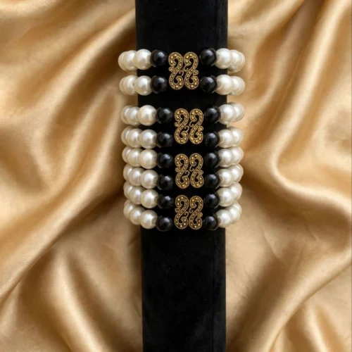 Double-strand faux pearl bracelets with black beads and antique gold-tone filigree links stacked on a black velvet display