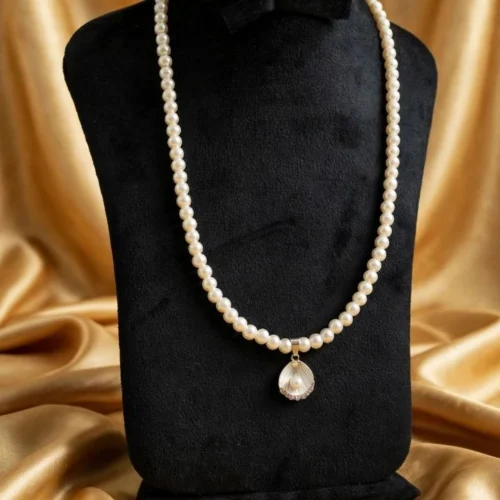 Long faux pearl necklace with a white shell pendant holding a small pearl on a black velvet bust against gold satin