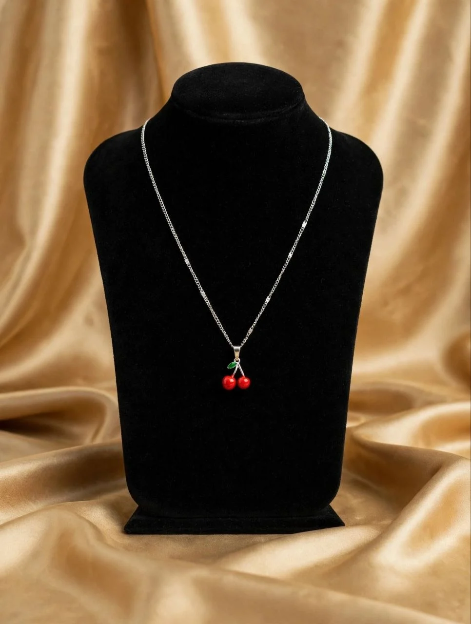 Red enamel cherry charm necklace on silver-tone curb chain displayed on black velvet bust