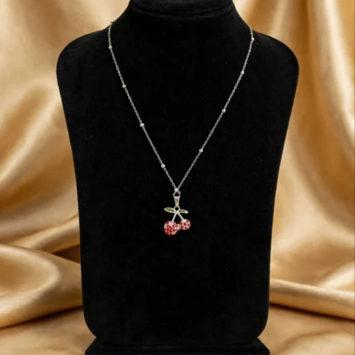 Red rhinestone cherry pendant with green leaves on silver-tone satellite chain on black velvet bust