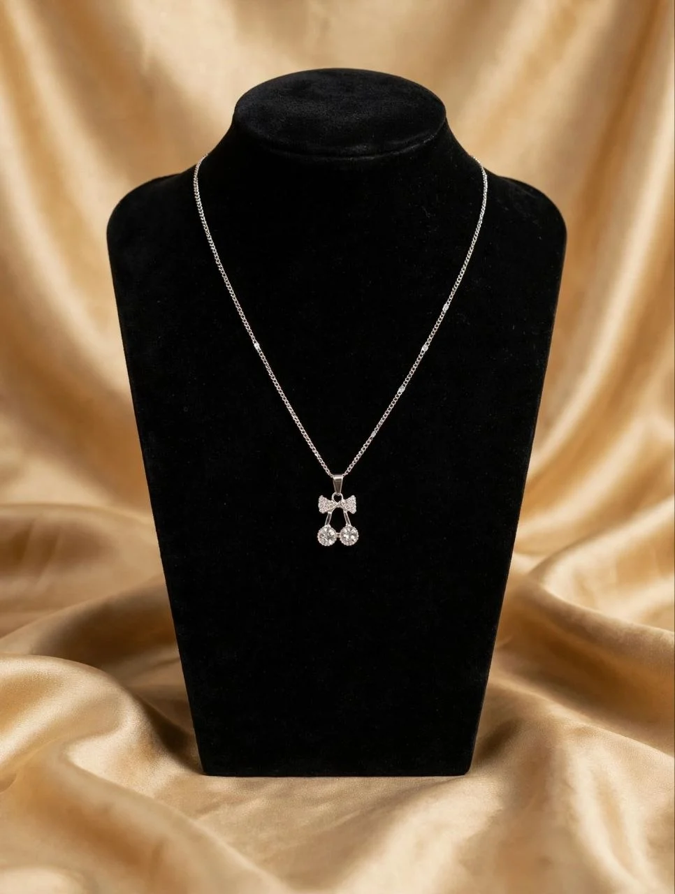 Silver-tone rhinestone bow and crystal cherry pendant necklace on black velvet bust