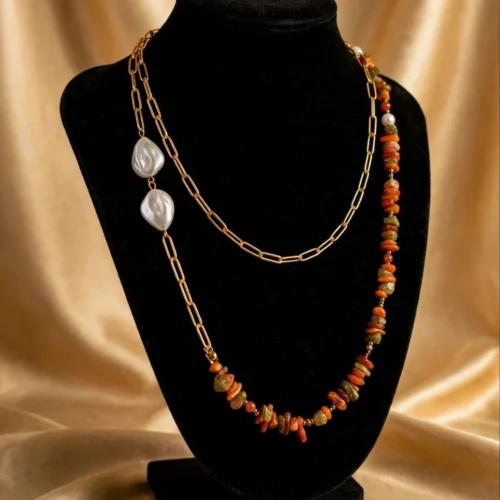 Layered gold-tone paperclip chain necklace with two baroque-look faux pearls and orange and green stone chips on black velvet bust