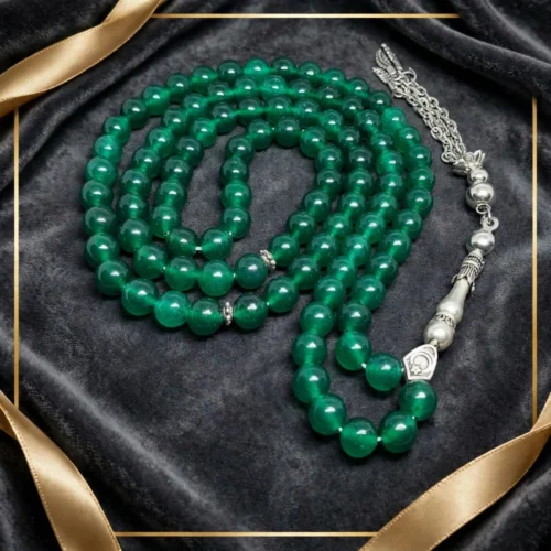 Emerald-green 99-bead misbaha with silver-tone crescent bead and chain tassel on dark velvet with gold ribbon