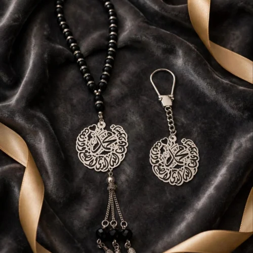 Black bead misbaha with silver-tone Arabic calligraphy medallion and matching calligraphy keychain on dark velvet with gold ribbon