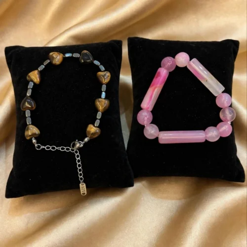Tiger-eye-look heart bracelet with clasp and pink agate-style tube bead stretch bracelet on two black velvet pillows