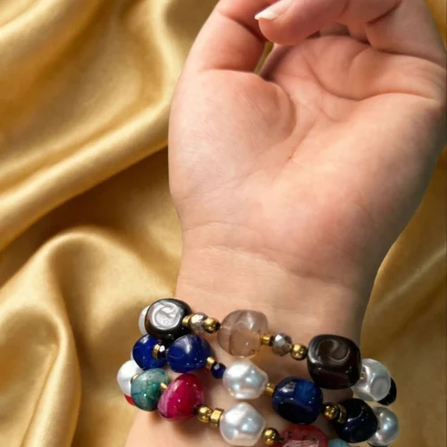 Multicolour agate-style stone and baroque-look faux pearl wrap bracelet coiled around a woman's wrist