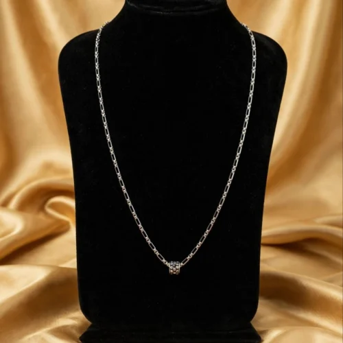 Silver-tone figaro chain necklace with black rhinestone barrel charm on black velvet bust