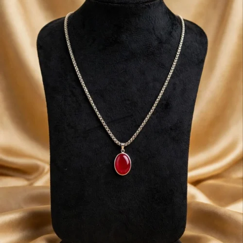 Bright red oval cabochon pendant on silver-tone box chain displayed on black velvet bust