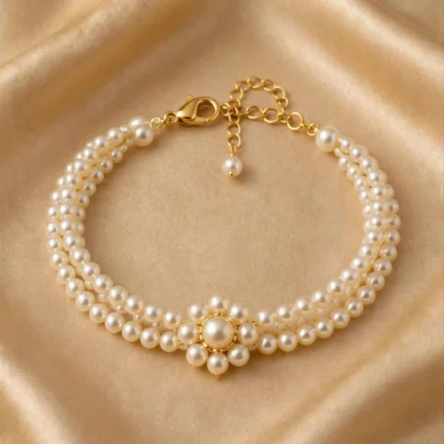 Multi-strand cream faux pearl bracelet with pearl flower centre and gold-tone lobster clasp on beige satin
