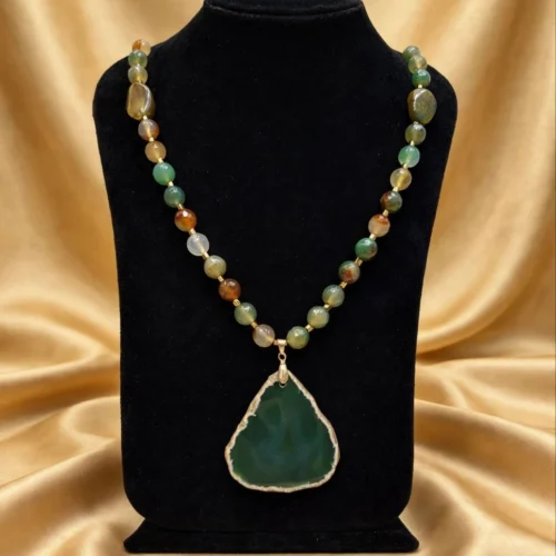 Green agate-style slice pendant on a necklace of green and amber stone beads on a black velvet bust