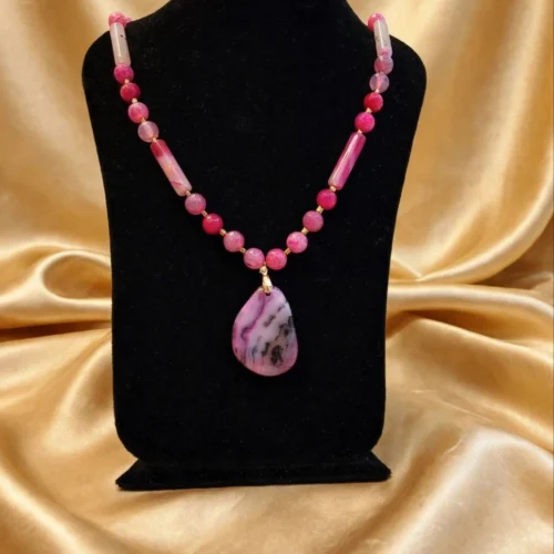 Pink faceted bead necklace with tube beads and pink agate-style teardrop pendant on a black velvet bust