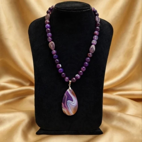 Purple faceted stone bead necklace with banded agate-style teardrop pendant on a black velvet bust