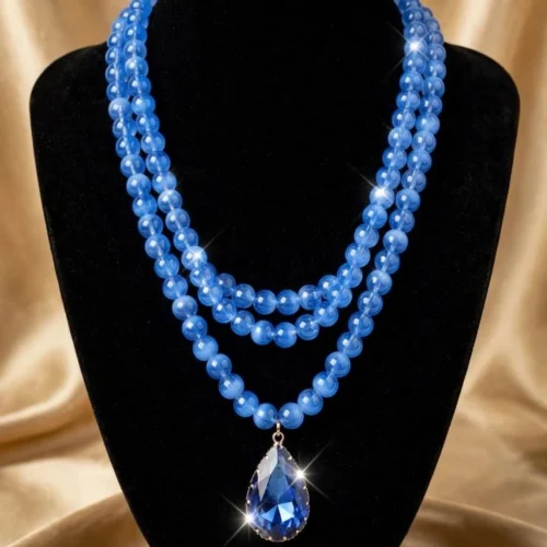 Triple-strand cornflower-blue bead necklace with large faceted blue crystal teardrop on a black velvet bust