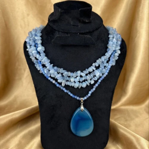 Multi-strand light blue stone chip necklace with blue agate-style teardrop pendant on a black velvet bust