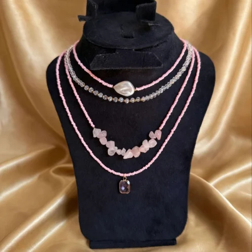 Four-layer pink seed bead necklace with faux pearl, crystal beads, pink stone chips and purple charm on a black velvet bust