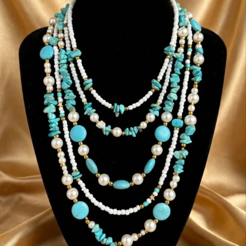 Five-strand necklace with turquoise-look chips and discs, white faux pearls and seed beads on a black velvet bust